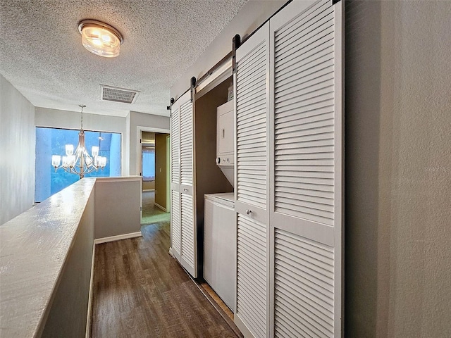 corridor featuring an inviting chandelier, a textured ceiling, a barn door, dark wood-type flooring, and stacked washer / dryer