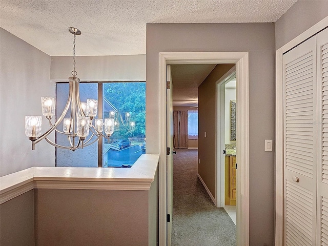 hall featuring an inviting chandelier, carpet floors, and a textured ceiling