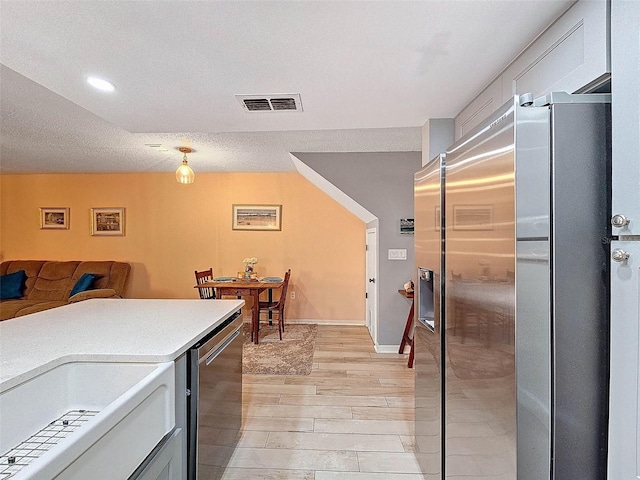 kitchen with visible vents, light wood-style flooring, light countertops, stainless steel refrigerator with ice dispenser, and open floor plan