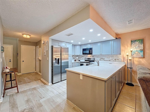 kitchen with backsplash, a textured ceiling, kitchen peninsula, stainless steel appliances, and light hardwood / wood-style flooring