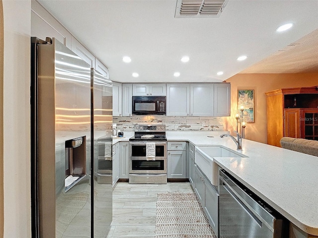 kitchen with sink, kitchen peninsula, stainless steel appliances, gray cabinets, and decorative backsplash