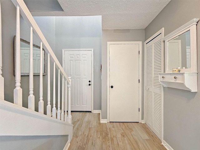 entryway with stairway, baseboards, a textured ceiling, and wood finished floors