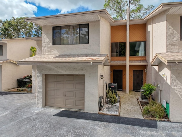 townhome / multi-family property with a shingled roof, an attached garage, central AC, and stucco siding