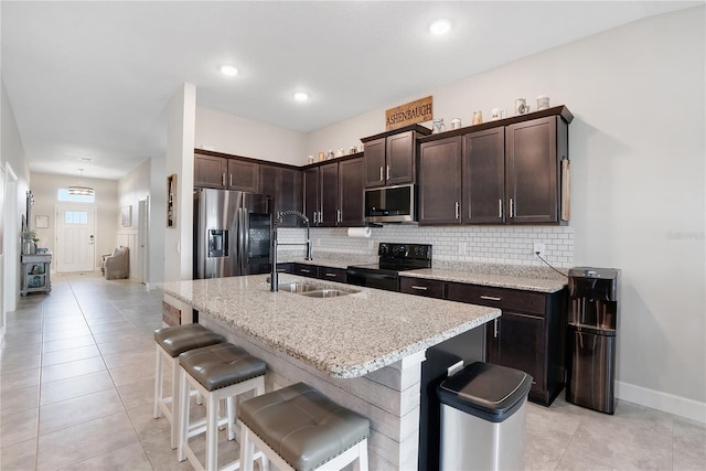 kitchen featuring an island with sink, dark brown cabinetry, a breakfast bar, sink, and appliances with stainless steel finishes