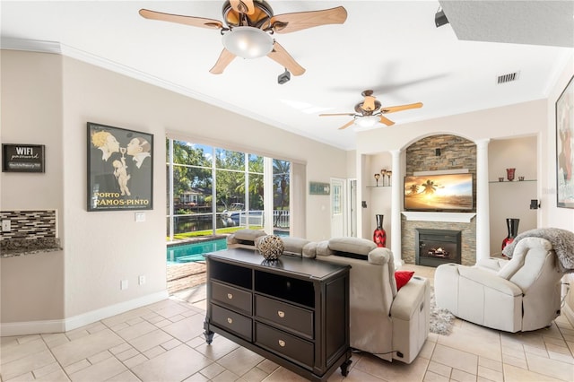 tiled living room featuring ceiling fan, crown molding, built in features, and a stone fireplace