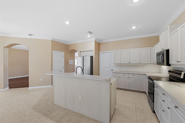 kitchen featuring appliances with stainless steel finishes, an island with sink, white cabinets, light tile patterned floors, and crown molding