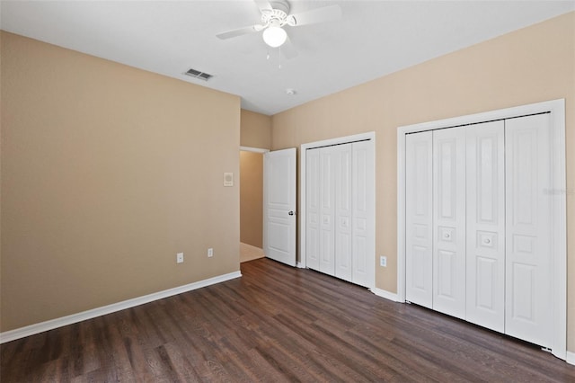 unfurnished bedroom featuring multiple closets, ceiling fan, and dark wood-type flooring