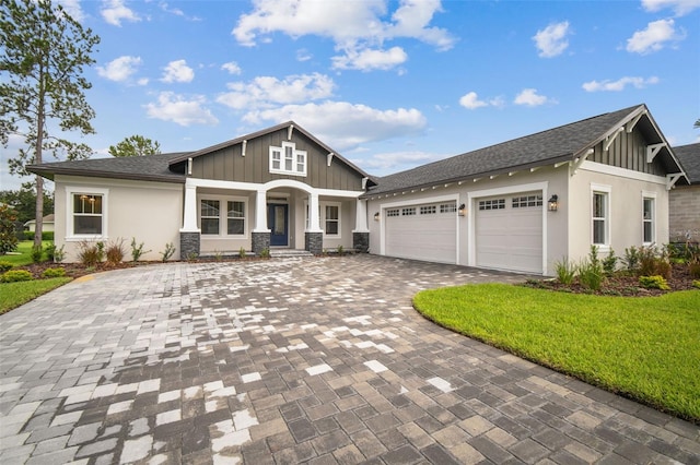 craftsman-style home with decorative driveway, roof with shingles, board and batten siding, a garage, and a front lawn