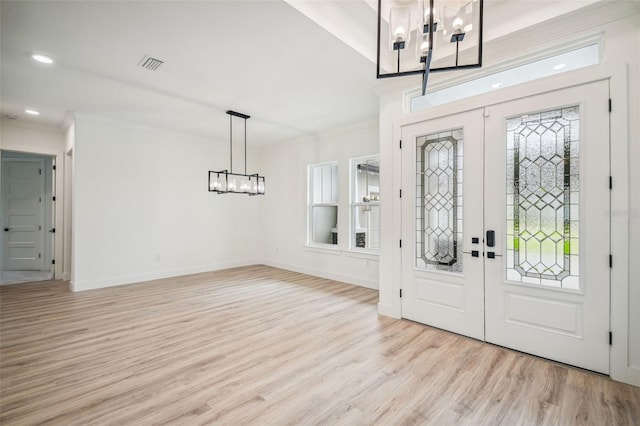 entrance foyer featuring french doors, ornamental molding, a notable chandelier, and light wood-type flooring