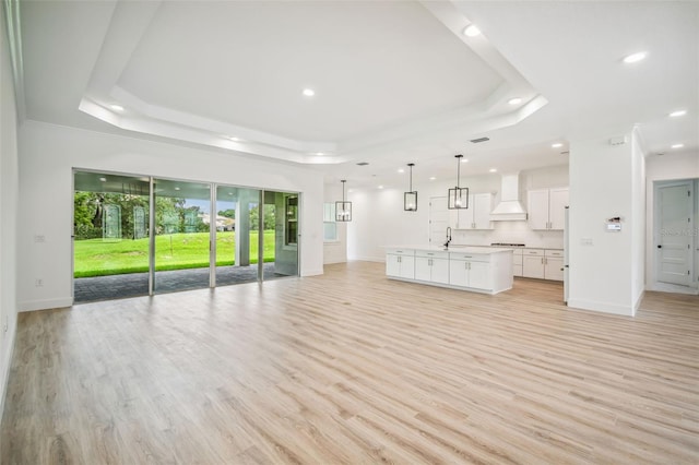 unfurnished living room with sink, light hardwood / wood-style flooring, and a tray ceiling