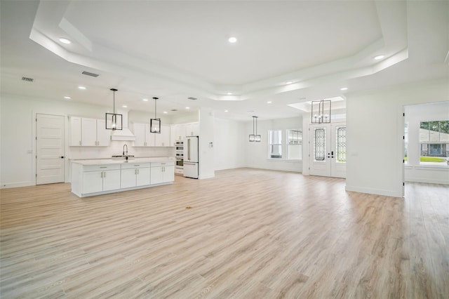 unfurnished living room with an inviting chandelier, sink, a tray ceiling, and light wood-type flooring