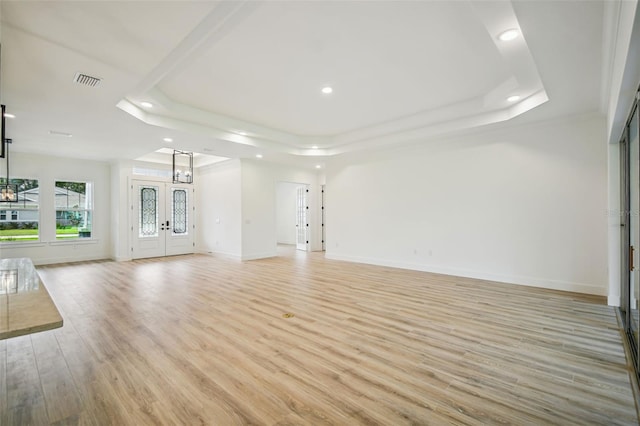 unfurnished living room featuring light hardwood / wood-style floors, french doors, and a raised ceiling