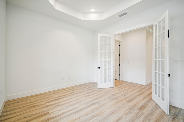 unfurnished room with french doors, a tray ceiling, and light hardwood / wood-style floors