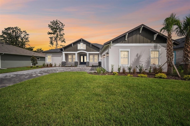 view of front of house with board and batten siding, decorative driveway, and a yard