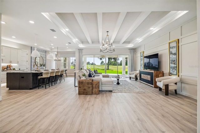 living room featuring light wood-style flooring, a chandelier, a decorative wall, and beamed ceiling