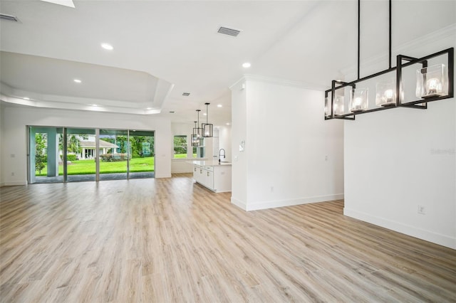 unfurnished living room with baseboards, light wood-style flooring, a tray ceiling, a sink, and recessed lighting