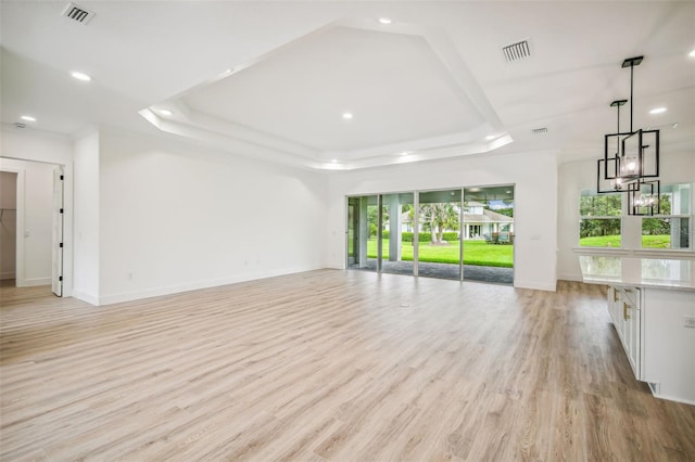 unfurnished living room featuring baseboards, a tray ceiling, visible vents, and light wood-style floors