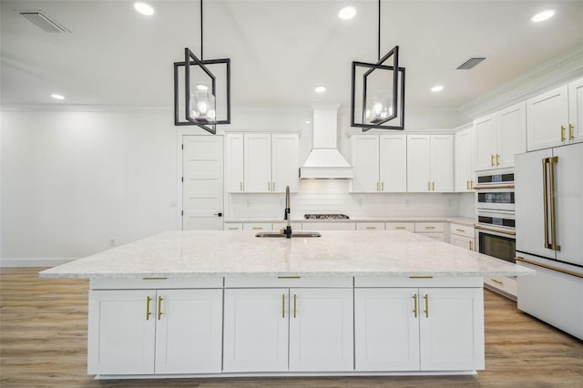 kitchen featuring custom exhaust hood, a sink, a kitchen island with sink, and white cabinets