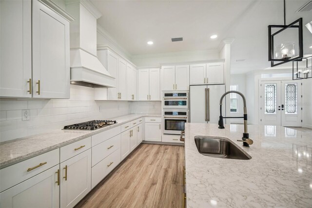 kitchen featuring stainless steel appliances, premium range hood, a sink, and light stone counters