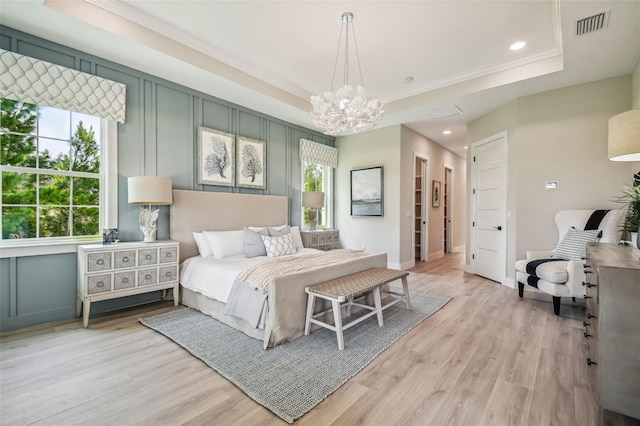 bedroom featuring light wood-style floors, a raised ceiling, visible vents, and a decorative wall