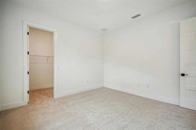 unfurnished bedroom with a walk in closet, visible vents, light carpet, and baseboards