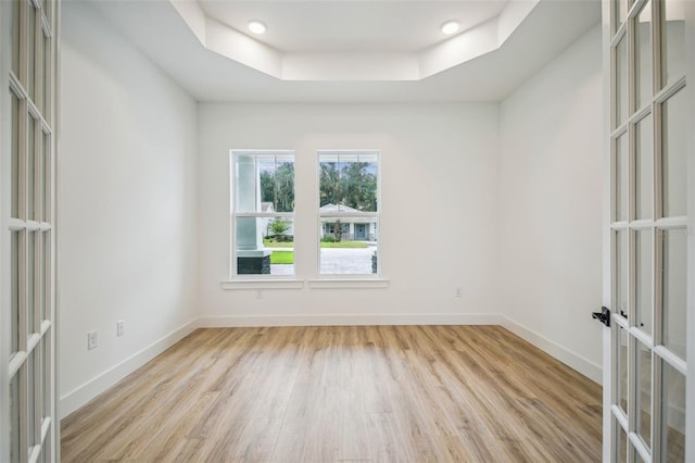 empty room featuring light wood-type flooring, french doors, a raised ceiling, and baseboards