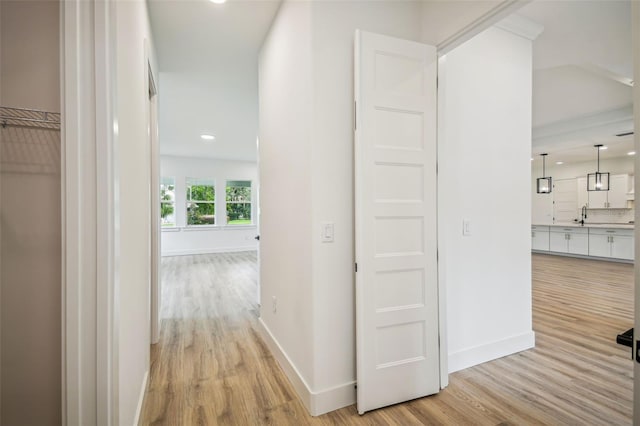 hall with light wood finished floors, baseboards, and a sink