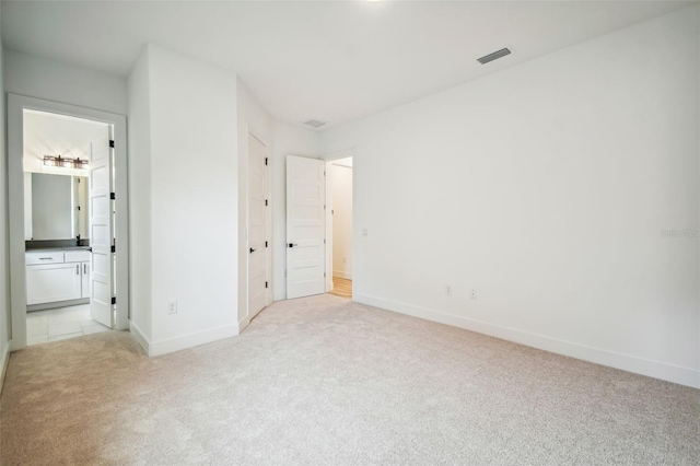 unfurnished bedroom featuring light colored carpet, ensuite bath, visible vents, and baseboards