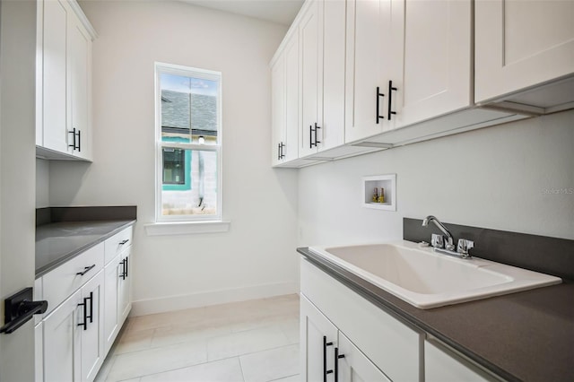 laundry area featuring washer hookup, light tile patterned floors, cabinet space, a sink, and baseboards