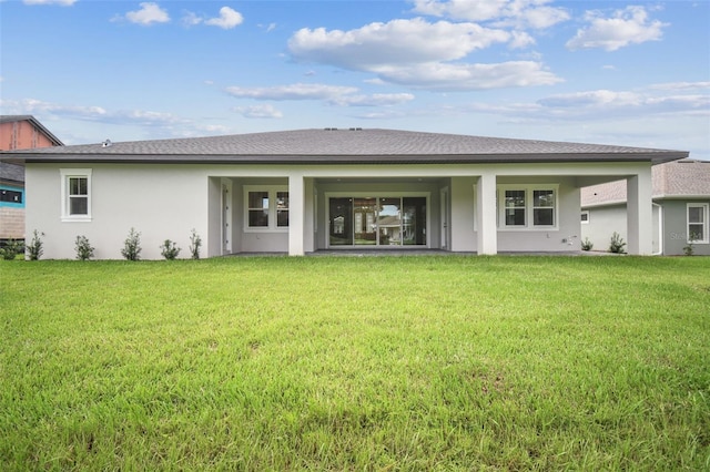 back of property with stucco siding, roof with shingles, and a yard