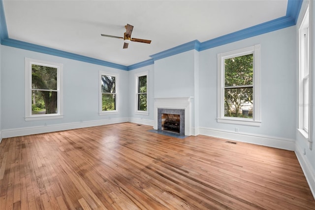 unfurnished living room featuring ceiling fan, ornamental molding, a tiled fireplace, and light hardwood / wood-style floors