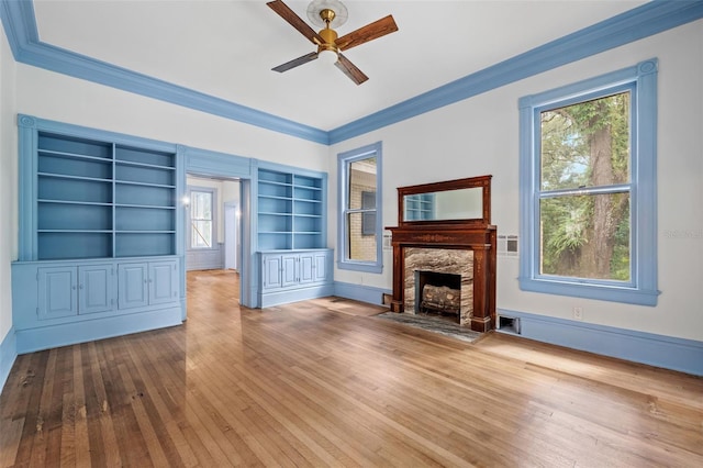 unfurnished living room with ceiling fan, built in features, hardwood / wood-style flooring, a fireplace, and crown molding