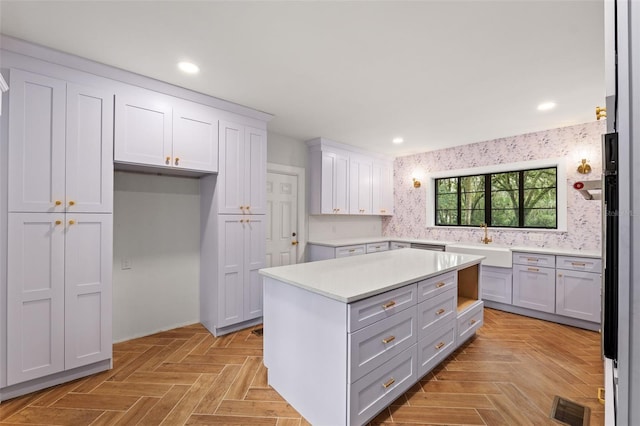 kitchen featuring decorative backsplash, white cabinets, light parquet flooring, a center island, and sink