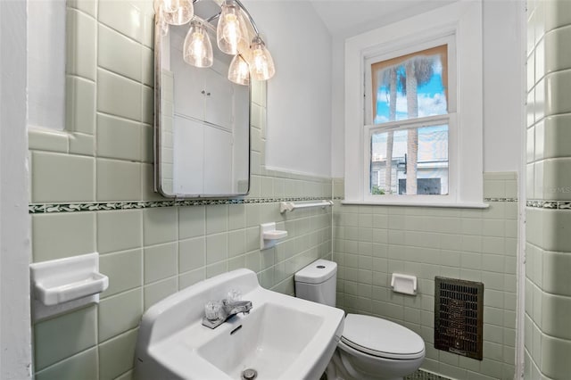 bathroom with tile walls, sink, heating unit, and toilet