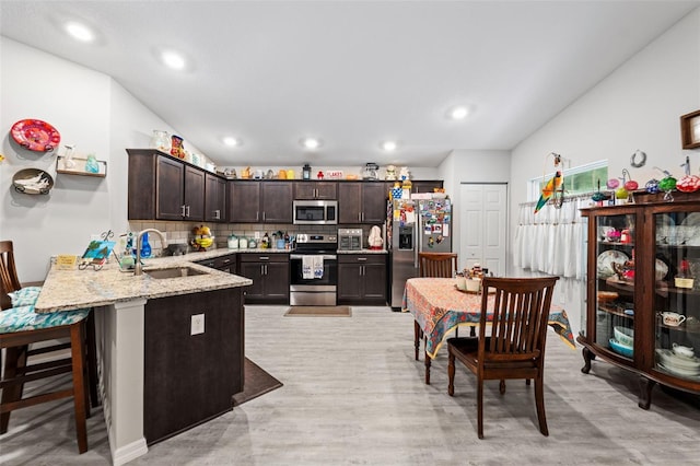 kitchen with sink, kitchen peninsula, decorative backsplash, stainless steel appliances, and dark brown cabinetry