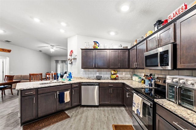 kitchen featuring appliances with stainless steel finishes, vaulted ceiling, kitchen peninsula, light wood-type flooring, and sink