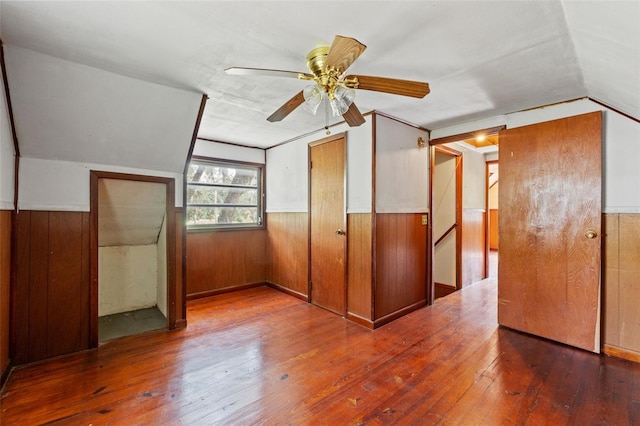 interior space with hardwood / wood-style floors, ceiling fan, wooden walls, and vaulted ceiling