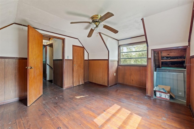 additional living space with ceiling fan, wooden walls, dark wood-type flooring, and vaulted ceiling