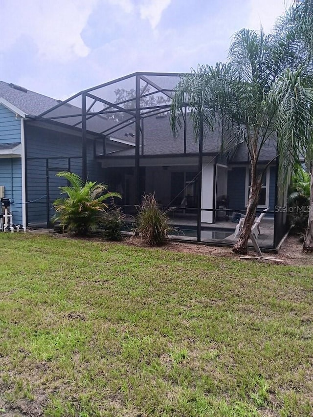 rear view of property with glass enclosure and a yard