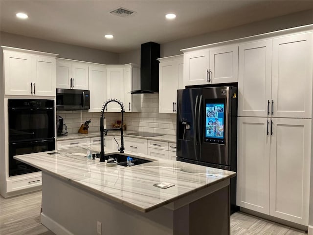 kitchen featuring black appliances, wall chimney range hood, an island with sink, and white cabinets