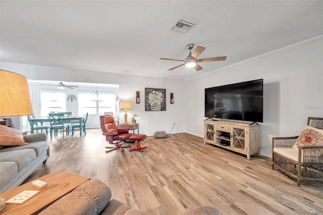 living room featuring ceiling fan, light hardwood / wood-style floors, ornamental molding, and a textured ceiling