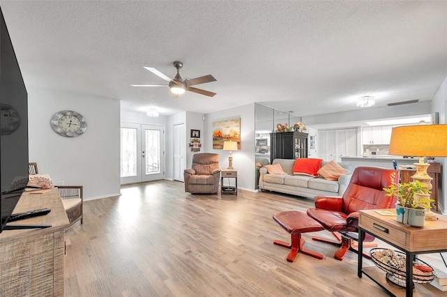 living room with french doors, light hardwood / wood-style floors, a textured ceiling, and ceiling fan