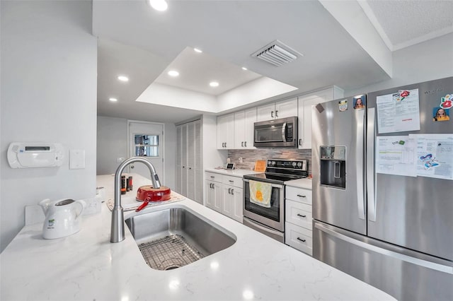 kitchen with light stone countertops, a raised ceiling, sink, white cabinetry, and appliances with stainless steel finishes