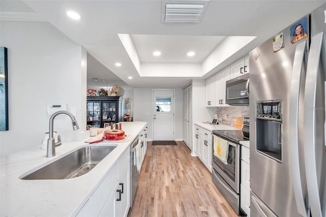 kitchen featuring light wood-type flooring, stainless steel appliances, a raised ceiling, white cabinets, and sink