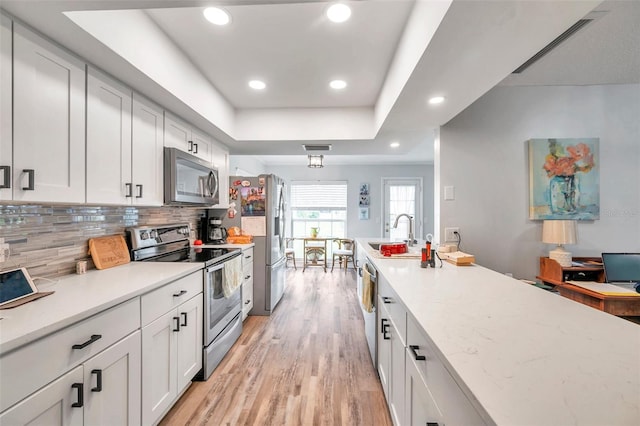 kitchen featuring sink, light hardwood / wood-style flooring, white cabinetry, stainless steel appliances, and decorative backsplash