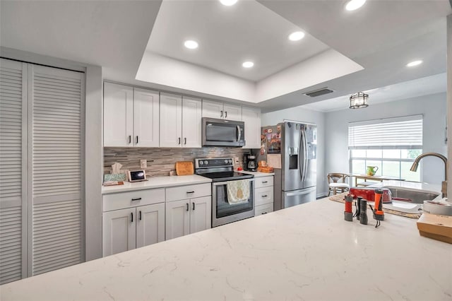 kitchen with sink, appliances with stainless steel finishes, a tray ceiling, and white cabinetry