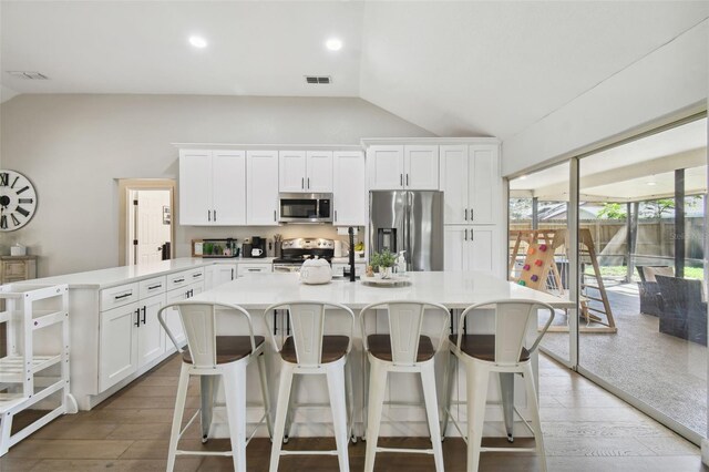 kitchen featuring light hardwood / wood-style flooring, a breakfast bar, lofted ceiling, appliances with stainless steel finishes, and white cabinetry