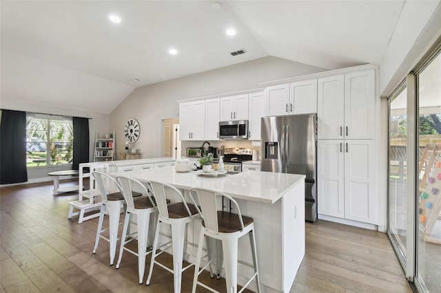 kitchen featuring appliances with stainless steel finishes, white cabinetry, vaulted ceiling, and light hardwood / wood-style flooring