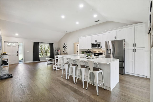 kitchen with white cabinets, an island with sink, appliances with stainless steel finishes, and lofted ceiling