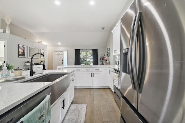 kitchen featuring light wood-type flooring, light stone countertops, lofted ceiling, stainless steel appliances, and white cabinetry